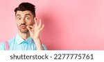 Small photo of Close up of funny caucasian guy touching his french moustache, pucker lips and looking silly, standing over pink background.