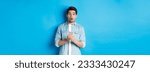 Small photo of Surprised man in casual clothes looking astounded, holding smartphone, standing against blue background.