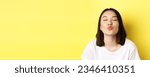Small photo of Valentines day concept. Close up of cute asian girl pucker lips and close eyes for kiss, standing romantic against yellow background.