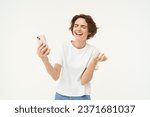 Small photo of Portrait of chatty young woman, laughing, using mobile phone, video chats online on smartphone, isolated over white background.
