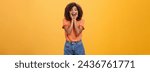 Small photo of Impressed talkative african american woman finding out hot details of rumor being excited, thrilled leaning face on palms, smiling broadly with amused expression listening carefully over orange wall.