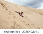 Small photo of A young boy is having great fun on an adventure activity in New Zealand called sand boarding. He is sliding dow a large sand dune.