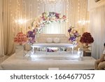 Small photo of A bridal dais of a malay wedding beautifully and brightly decorated with pastel colored flowers and lights with a white bench to harmonised between each elements.