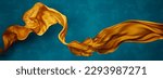 Small photo of Yellow silk fabric floating in front of blue background wall. Flying satin scarf abstract shape. Luxury fashion aesthetic.