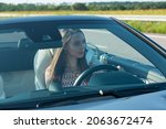 Beautiful young woman driving a Mercedes Benz SL550 convertible on the road. The girl is very attentive and focused while driving.