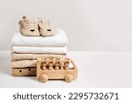Small photo of Stack of baby clothes with baby shoes and wooden toy car. Cotton clothes and muslin swaddle blanket in pastel colors. Clean freshly laundered, neatly folded kids clothes.