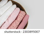 Small photo of Stack of baby clothes in the basket. Cotton clothes and muslin swaddle blanket in pastel colors. Clean freshly laundered, neatly folded kids clothes. Close up