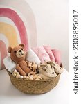 Small photo of Basket with baby stuff and accessories for newborn. Gift basket with cotton clothes and muslin swaddle blanket, baby shoes, toys and cute teddy bear in beige colors.