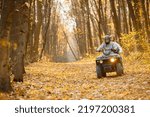 Small photo of Man and woman driving quad bike in autumn forest