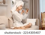 Woman wearing dressing gown and has a towel on her hair doing a make up