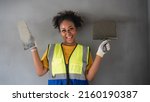 Small photo of Portrait of an attractive African-American woman standing with plastering tool.engineer at grey cement wall. Female worker,wall decoration specialist.Smiling confidently. expert skim coat,plastering