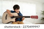 Small photo of sian Teen boy sitting on the bed at home while practicing acoustic guitar.