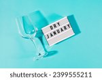 Text Dry January on the decorative lightbox and empty wine glass isolated on blue background, top view