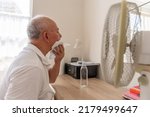 Small photo of A senior man suffering from extreme hot, record breaking summer heat, trying to keep cool and well at home.
