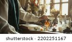 Small photo of A close-up of a perfumer at his desk looking for a new fragrance. Vintage cinematic perfumery concept. Sunny day in the working workshop. Lots of ingredients, glass flasks. Depth of field