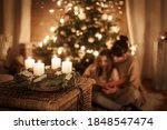 Child sits with mother in front of the Christmas tree and read a book together and look forward to X-Mas, advent wreath