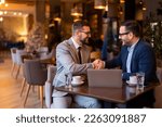Small photo of Two elegant stylish corporate leaders shaking hands after a successful business meeting in a restaurant in the evening. Proud business partners shaking hands while sitting at table in restaurant.