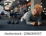 Small photo of Beautiful happy smiling young woman in comfortable sports clothes feeling motivated determined to work on her body weight to stay active, healthy and in shape practicing plank exercise at gym.