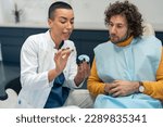 Small photo of Female dentist orthodontist holding dental impression imprints of patient's teeth, gums and oral structures, talking about dental restorations future procedures during appointment at dentist's office.