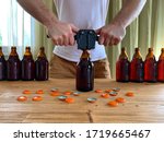 Small photo of Craft beer brewing at home, man closes brown glass beer bottles with plastic capper on wooden table with orange crown caps. Horizontal image