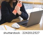 A woman working at a desk using a laptop and a mouse is suffering from wrist pain, and the painful part is marked in red