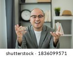 Small photo of A man around the age of 35. Working at home by meeting video conference looking at camera. He was wearing a grey suit and glasses. Asian businessman work from home talking on screen.
