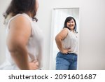 Small photo of Body positive plus size female clothing. Body positive plus size woman happily and is proud of herself looking at mirror at home. Try wearing clothes that measure the size.