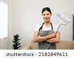 Young beautiful woman with apron and rubber glove ready for cleaning home background. Housekeeping housework or maid worker holding broom