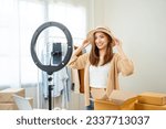 Small photo of Young asian woman business owner at fashion store using cellphone live streaming for sale fashion hat and clothing. Influencers record video review item for sell on social media. Online shopping