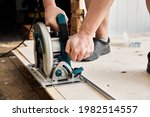 Small photo of Sawing plywood by circular saw. Home repair. Hand tool. Man hold equipment. Building process. Woodworking. Safety engineering. Without gloves. Copy space. Indoor. Cutting material. Rental instrument.
