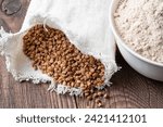 Small photo of Buckwheat in a canvas bag and buckwheat flour in a bowl on a wooden table. Gluten free buckwheat flour.