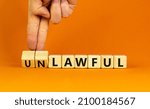 Small photo of Lawful or unlawful symbol. Businessman turns wooden cubes and changes the word unlawful to lawful. Beautiful orange table, orange background, copy space. Business and lawful or unlawful concept.