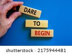Small photo of Dare to begin symbol. Wooden blocks with words 'Dare to begin'. Beautiful blue background, businessman hand. Business, dare to begin concept, copy space.