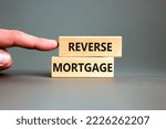 Small photo of Reverse mortgage symbol. Concept words Reverse mortgage on wooden blocks. Beautiful grey table grey background. Businessman hand. Business and reverse mortgage concept. Copy space.