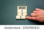 Small photo of Time to grade 3 symbol. Concept word Grade 1 2 3 on wooden block. Businessman hand. Beautiful grey table grey background. Business planning and time to grade 3 concept. Copy space.