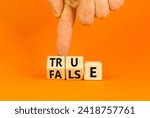 Small photo of False or true symbol. Turned wooden cubes and changed the word false to true or vice versa. Beautiful orange table, orange background, copy space. Businessman hand. Business and false or true concept.