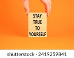 Small photo of Stay true to yourself symbol. Concept word Stay true to yourself on beautiful wooden block. Beautiful orange table background. Businessman hand. Business stay true to yourself concept. Copy space