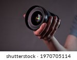 Modern digital camera lens in hand close up over dark background.
