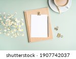 Top view blank paper Notebook, flowers, golden paper binder clips, cup of coffee and pen. Desktop mock up, Flat lay of green working table background with office equipment, mockup greeting card