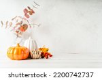 Small photo of Details of Still life, pumpkins, candle, brunch with leaves on white table background, home decor in a cozy house. Autumn weekend concept. Fallen leaves and home decoration