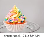Rainbow Iced Birthday cupcake on a stand over light grey background.