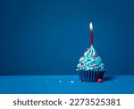 Blue cupcake with red sprinkles and lit candle on a blue background.