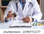 Small photo of male medicine doctor hand holds the bottle of pills and writes a prescription to the patient at the worktable. Panacea and life save, prescribing treatment legal drug store concept.