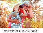 Little girl with her grandmother looking through binoculars outdoor. Discovery, adventure, having fun time with family. Birdwatching