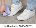 Cleaning white shoes, caring for sneakers. A woman wipes her leather shoes with a wet cloth from dust and dirt