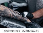 Close up tattooist cleaning fresh tattoo. Final process on forearm with white ink. Detail black gloves tattooing. Tattoo artist working in studio. Creative small business and tattoo master.