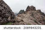 The top of the mountain has rocky soil. Fancy pointed stones against a cloudy sky. Colorful lichens grow on boulders. Kamchatka. Mount Camel