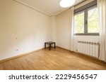 Empty living room with French oak parquet floors with plain white painted walls and a window with a radiator and white curtains