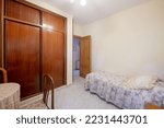 Bedroom with small bed with ugly patterned bedspread and large built-in wardrobe with sliding doors made of dark varnished wood