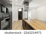 Small photo of studio with an open kitchen with an island with black furniture, a wooden worktop with a sink and a hob under the extractor hood and light laminated flooring and a black door to the street